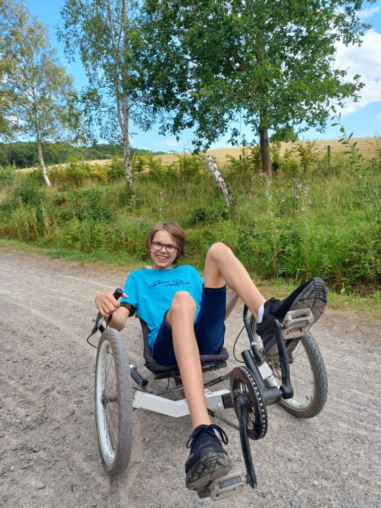 Boy in a blue t-shirt smiling while riding a two-wheeled vehicle outdoors, representing children with EHCP.