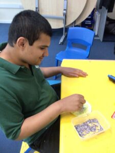 Child sitting at a yellow table, smiling and playing with beads, representing children with disabilities.