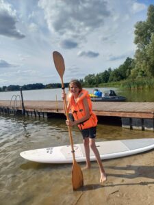 Child standing by a river with a paddle and wearing a life jacket, representing children with disabilities.