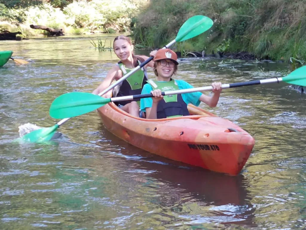 Boy and girl smiling while paddling in a canoe on a river, enjoying time together as children with disabilities.