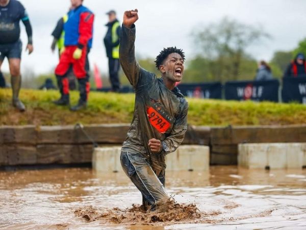 Boy running through mud with his arm raised in victory, participating in a race, representing children with disabilities.