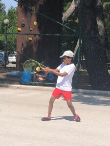 Boy playing tennis on a court wearing a white t-shirt, orange shorts, and a white baseball cap, representing children with ADHD.